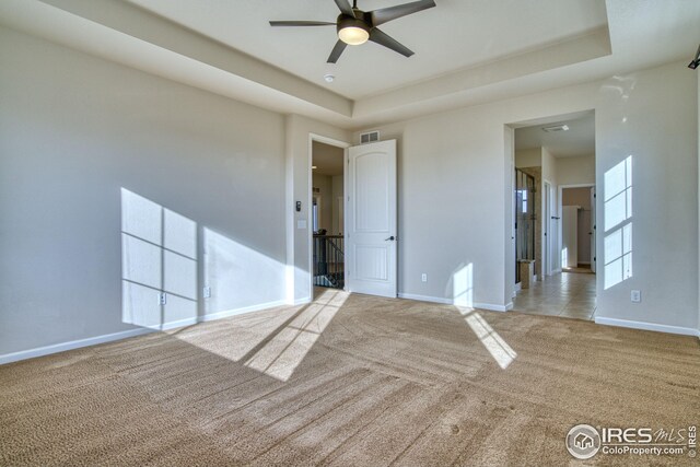 carpeted empty room featuring ceiling fan and a raised ceiling