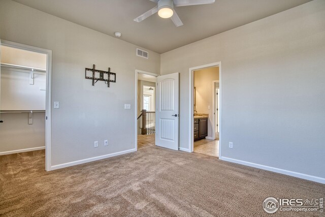 unfurnished bedroom featuring light carpet, a walk in closet, a closet, and ceiling fan