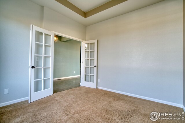 carpeted spare room featuring a raised ceiling and french doors