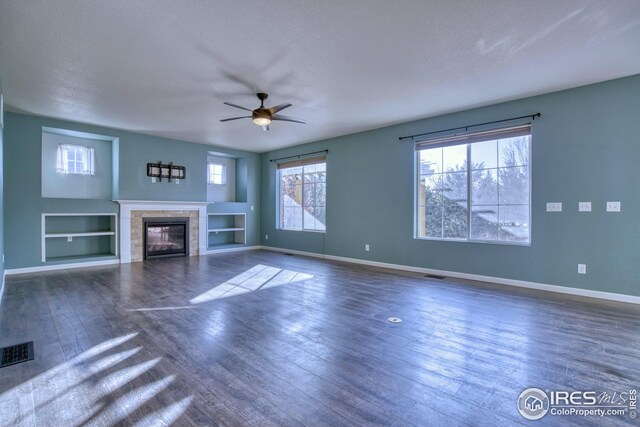 unfurnished living room with a tile fireplace, built in shelves, a textured ceiling, and dark wood-type flooring