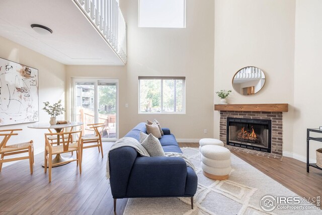 living room featuring a towering ceiling, a fireplace, baseboards, and wood finished floors