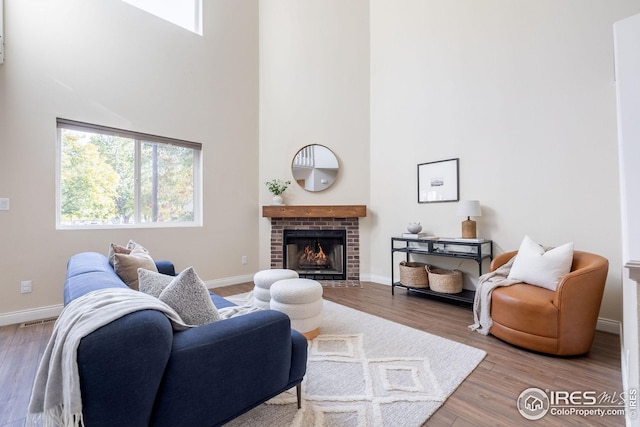 living room featuring a fireplace, baseboards, a towering ceiling, and wood finished floors