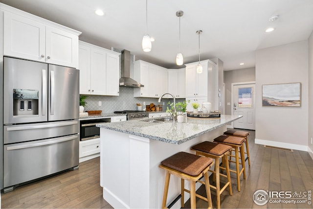 kitchen with light stone countertops, appliances with stainless steel finishes, wall chimney range hood, a sink, and dark wood-type flooring