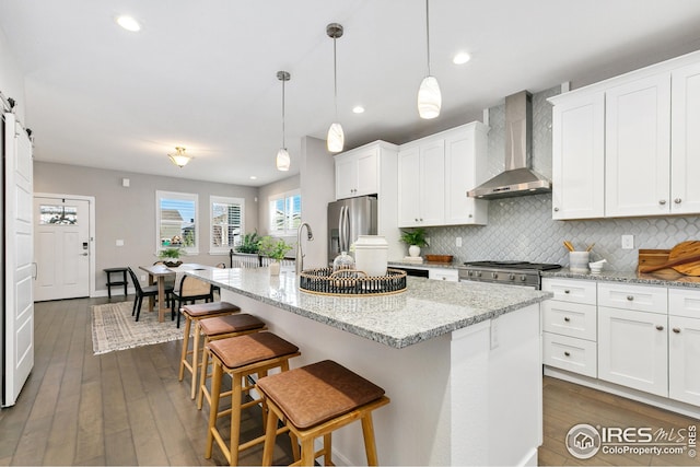 kitchen featuring stove, stainless steel fridge, wall chimney range hood, white cabinets, and backsplash