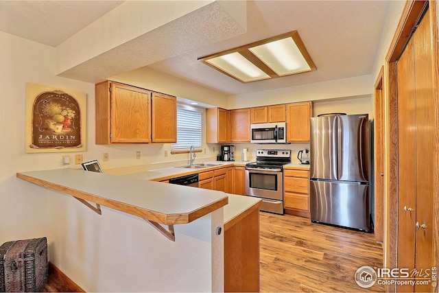 kitchen featuring sink, appliances with stainless steel finishes, a kitchen breakfast bar, kitchen peninsula, and light hardwood / wood-style floors