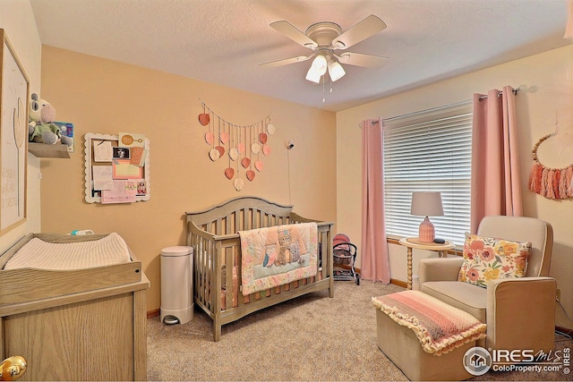 bedroom featuring a textured ceiling, light colored carpet, a nursery area, and ceiling fan