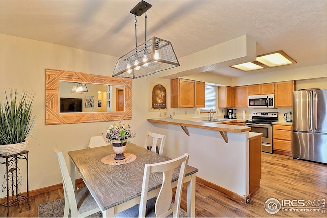 kitchen featuring hanging light fixtures, light hardwood / wood-style flooring, appliances with stainless steel finishes, a kitchen breakfast bar, and kitchen peninsula