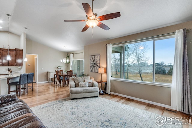 living room featuring light hardwood / wood-style flooring, ceiling fan with notable chandelier, and lofted ceiling