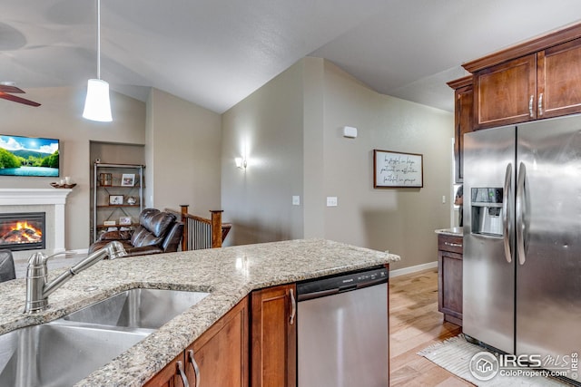 kitchen with sink, stainless steel appliances, light stone counters, vaulted ceiling, and decorative light fixtures