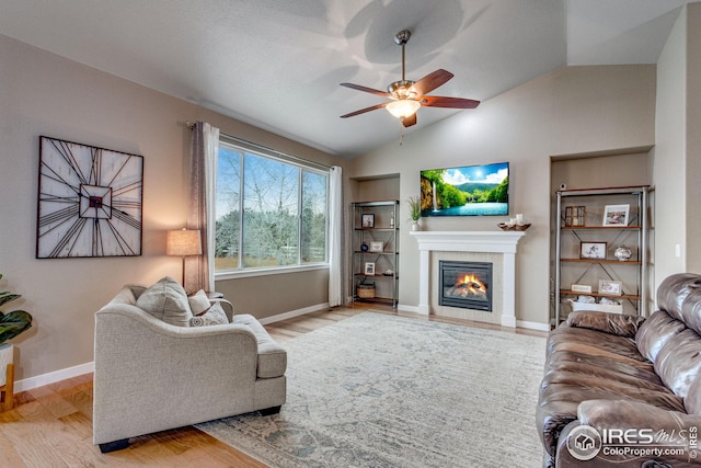 living room with a tile fireplace, ceiling fan, built in features, vaulted ceiling, and light wood-type flooring