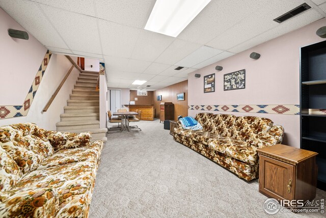 living room with a drop ceiling, wood walls, and light colored carpet