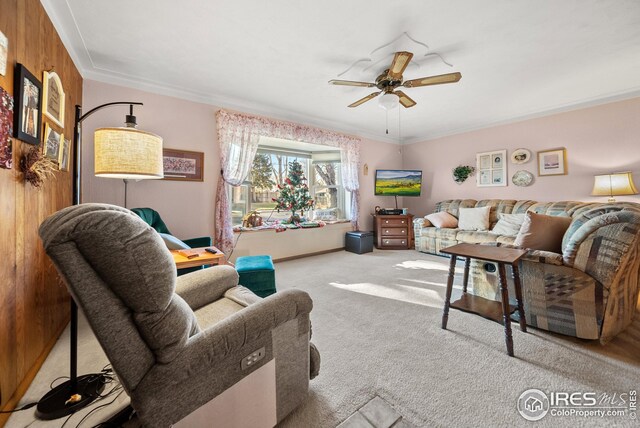 carpeted living room featuring crown molding, wooden walls, and ceiling fan