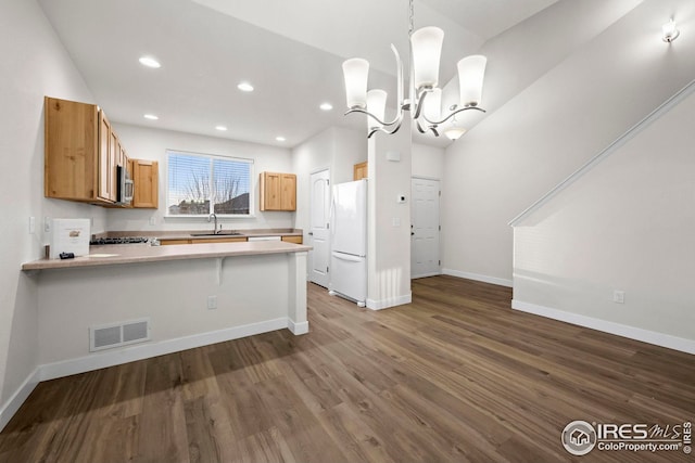 kitchen featuring kitchen peninsula, dark wood-type flooring, sink, white refrigerator, and hanging light fixtures