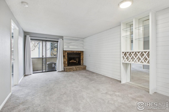 unfurnished living room with a textured ceiling, light colored carpet, a stone fireplace, and wooden walls