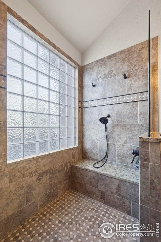 bathroom with a tile shower, lofted ceiling, and a healthy amount of sunlight