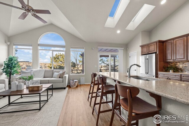 kitchen with high quality fridge, light stone counters, a skylight, a breakfast bar, and light wood-style flooring