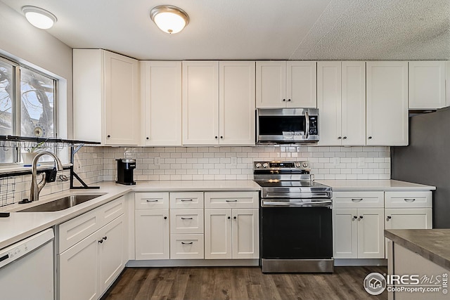 kitchen with appliances with stainless steel finishes, dark wood-style flooring, white cabinets, and a sink