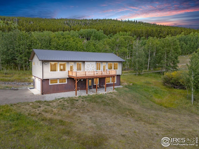 view of front of property featuring a deck, driveway, an attached garage, and a view of trees