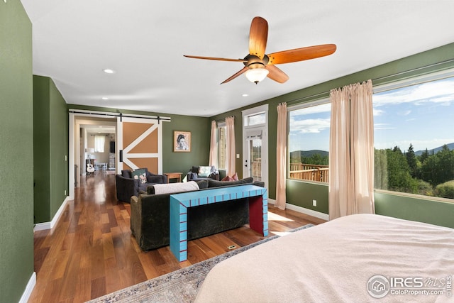 bedroom with a barn door, recessed lighting, wood finished floors, access to exterior, and baseboards