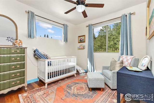 bedroom with a nursery area, multiple windows, a ceiling fan, and wood finished floors