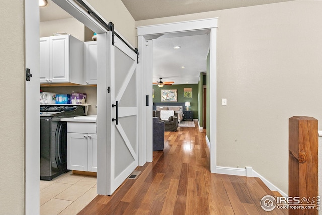 hallway featuring light wood finished floors, a barn door, visible vents, baseboards, and washer / clothes dryer