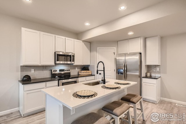 kitchen with a kitchen island with sink, white cabinets, sink, a kitchen bar, and stainless steel appliances