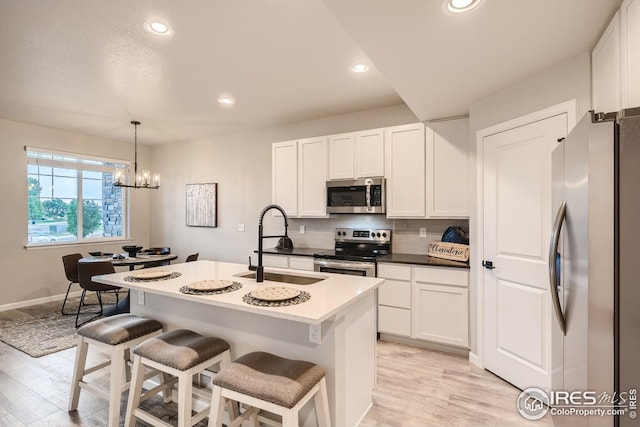 kitchen featuring white cabinetry, hanging light fixtures, an island with sink, a breakfast bar, and appliances with stainless steel finishes