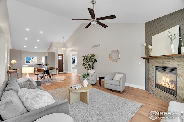 living room with a stone fireplace, ceiling fan, high vaulted ceiling, and light wood-type flooring