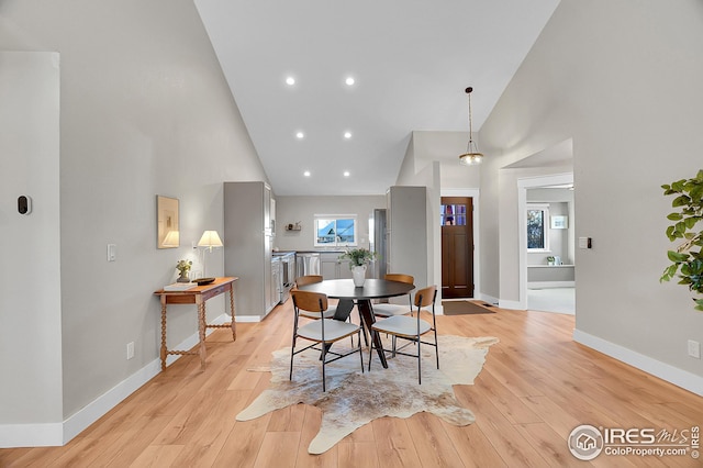 dining area with high vaulted ceiling and light hardwood / wood-style floors