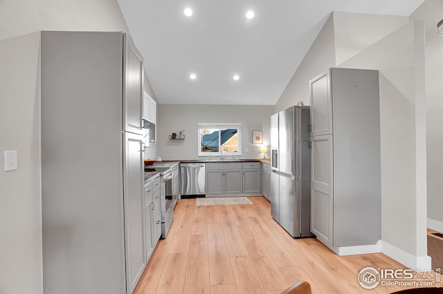 kitchen with gray cabinetry, sink, vaulted ceiling, appliances with stainless steel finishes, and light wood-type flooring