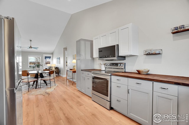 kitchen featuring vaulted ceiling, ceiling fan, light wood-type flooring, butcher block counters, and stainless steel appliances