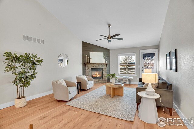 living room featuring hardwood / wood-style floors, ceiling fan, a stone fireplace, and high vaulted ceiling