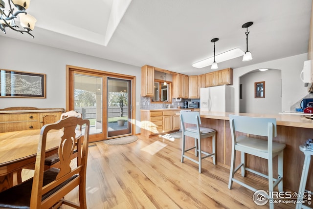 kitchen featuring white appliances, hanging light fixtures, light brown cabinetry, decorative backsplash, and light wood-type flooring