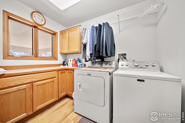 clothes washing area with cabinets, washing machine and clothes dryer, and light hardwood / wood-style flooring