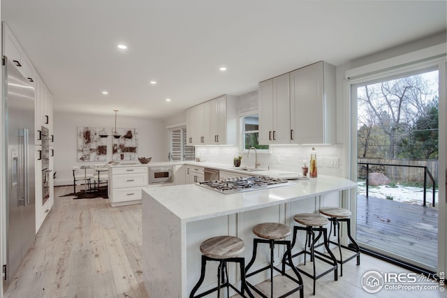 kitchen with kitchen peninsula, appliances with stainless steel finishes, sink, decorative light fixtures, and white cabinetry