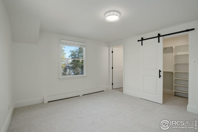 unfurnished bedroom with light carpet, a barn door, a baseboard radiator, a spacious closet, and a closet