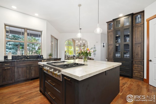 kitchen featuring dark hardwood / wood-style flooring, dark brown cabinetry, decorative light fixtures, a kitchen island, and stainless steel gas stovetop