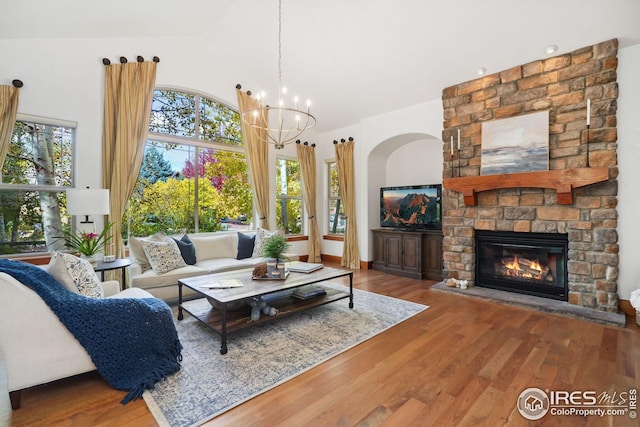 living room with a stone fireplace, wood-type flooring, lofted ceiling, and a notable chandelier