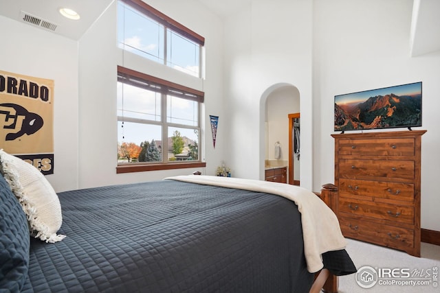 carpeted bedroom with a towering ceiling and ensuite bath
