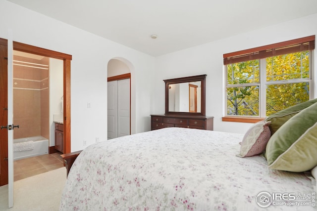 bedroom featuring light tile patterned floors, connected bathroom, and a closet
