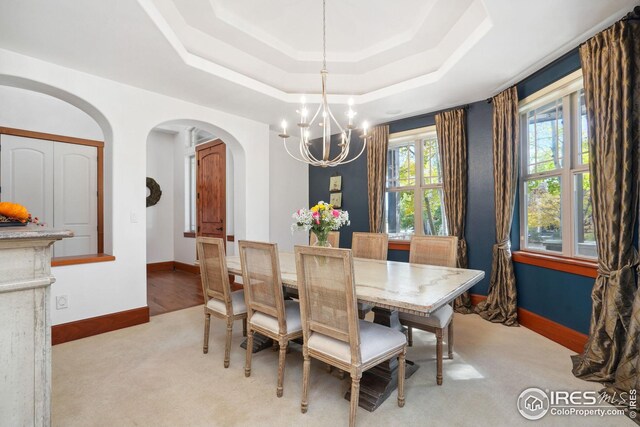 carpeted dining space with an inviting chandelier and a tray ceiling