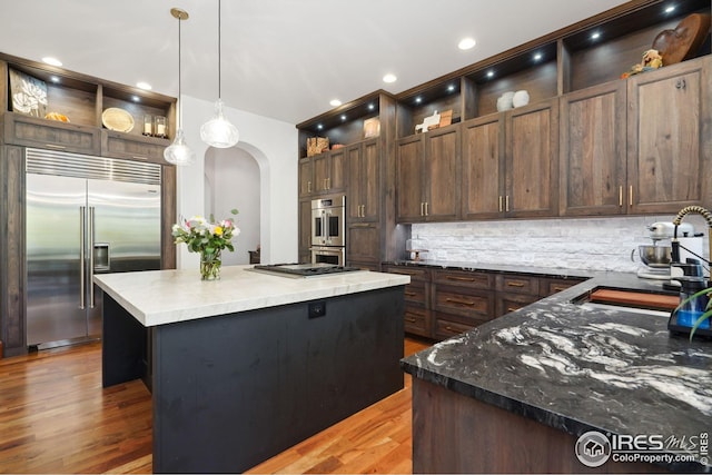 kitchen featuring pendant lighting, decorative backsplash, dark brown cabinets, a kitchen island, and appliances with stainless steel finishes