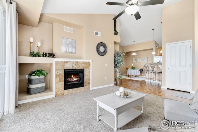 living room with a tiled fireplace, ceiling fan, high vaulted ceiling, and light colored carpet