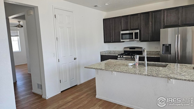 kitchen with sink, hardwood / wood-style flooring, light stone countertops, dark brown cabinets, and stainless steel appliances