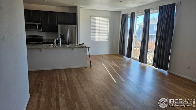 kitchen featuring sink, a kitchen breakfast bar, light stone counters, hardwood / wood-style floors, and appliances with stainless steel finishes