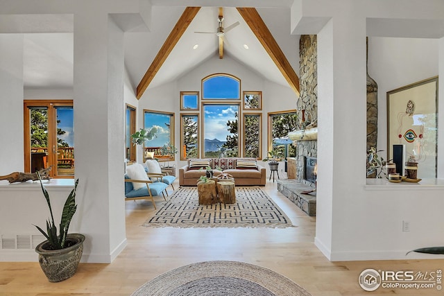 living room featuring wood finished floors, baseboards, high vaulted ceiling, beam ceiling, and a stone fireplace