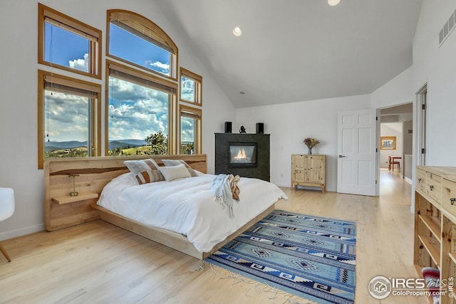 bedroom featuring visible vents, baseboards, light wood finished floors, high vaulted ceiling, and a multi sided fireplace