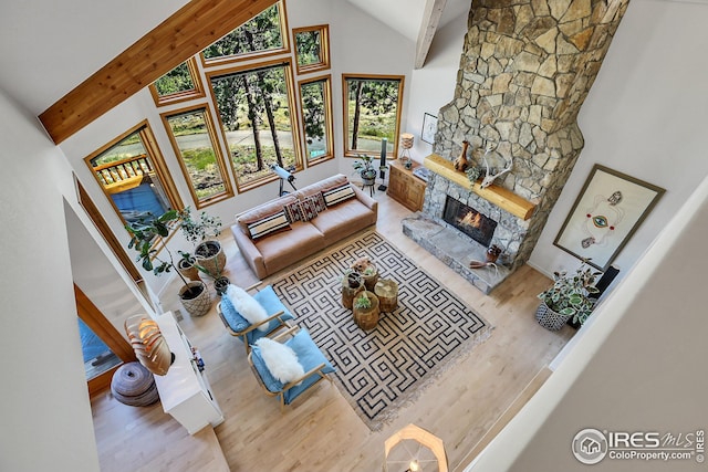 living area featuring a stone fireplace, beamed ceiling, high vaulted ceiling, and wood finished floors