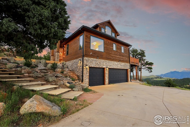 view of property exterior with driveway, stone siding, stairway, a mountain view, and a garage