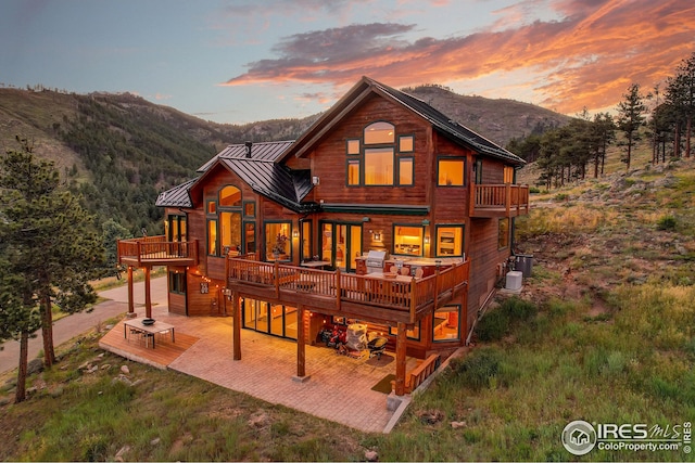 rear view of house featuring central AC unit, a patio, metal roof, a deck with mountain view, and a standing seam roof